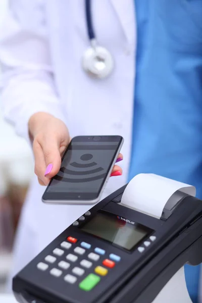 Le docteur tient le terminal de paiement entre les mains. Payer pour les soins de santé. Docteur. — Photo