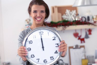 Mutlu genç kadın Noel süslemeli mutfakta saat gösteriyor.