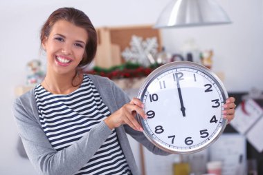 Mutlu genç kadın Noel süslemeli mutfakta saat gösteriyor.