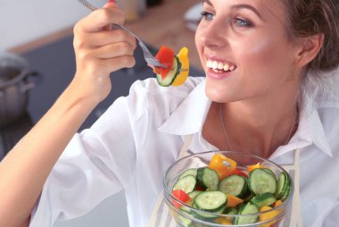 Genç kadın modern mutfakta taze salata yiyor.