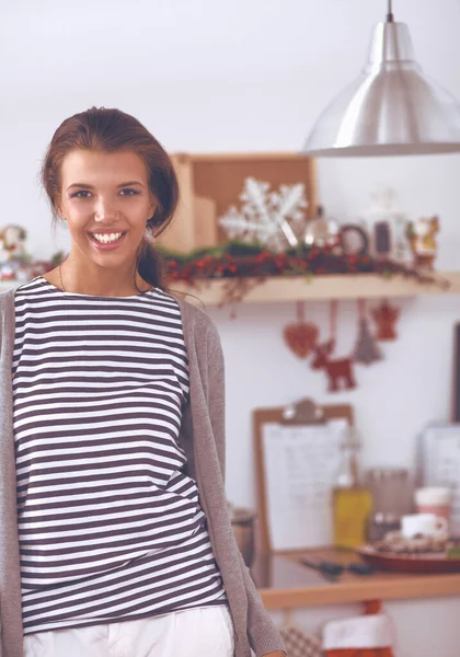 Glimlachende jonge vrouw in de keuken, geïsoleerd op kerst achtergrond — Stockfoto