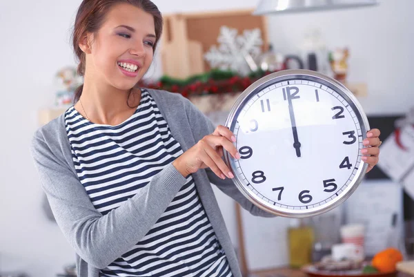 Happy young woman showing clock in christmas decorated kitchen — Stock Photo, Image