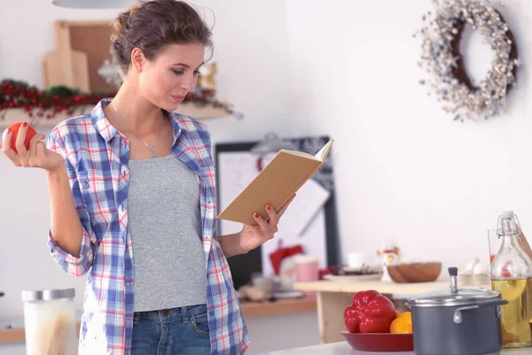 Jonge vrouw die kookboek leest in de keuken, op zoek naar recept — Stockfoto