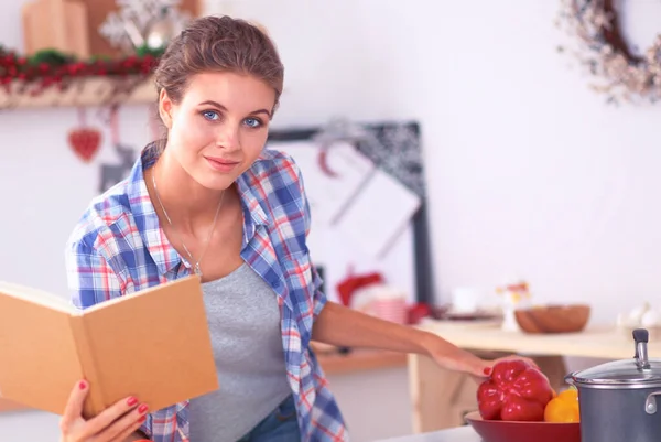 Ung kvinna läser kokbok i köket, letar efter recept — Stockfoto