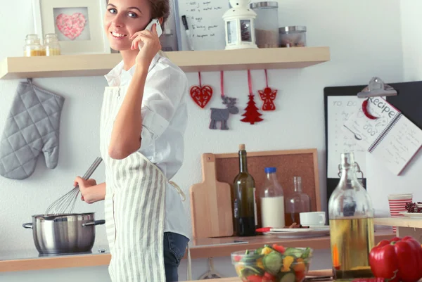 Portret van een lachende vrouw met telefoon in de keuken thuis — Stockfoto