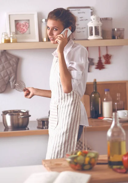 Porträtt en leende kvinna med telefon av grönsaker i köket hemma — Stockfoto