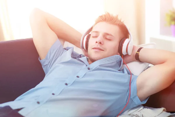 Een jonge knappe man op de bank luisterend naar muziek — Stockfoto