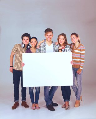 Beyaz arka planda izole edilmiş boş bir tahta tutan bir grup genç arkadaş.