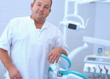 Diş kliniğinde duran gülümseyen bir dişçinin portresi.