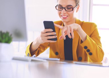 Dizüstü bilgisayarın önünde otururken cep telefonu ve mesaj kullanan bir iş kadınının portresi