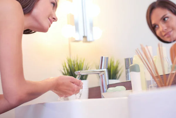 Молодая женщина умывается чистой водой в ванной комнате — стоковое фото
