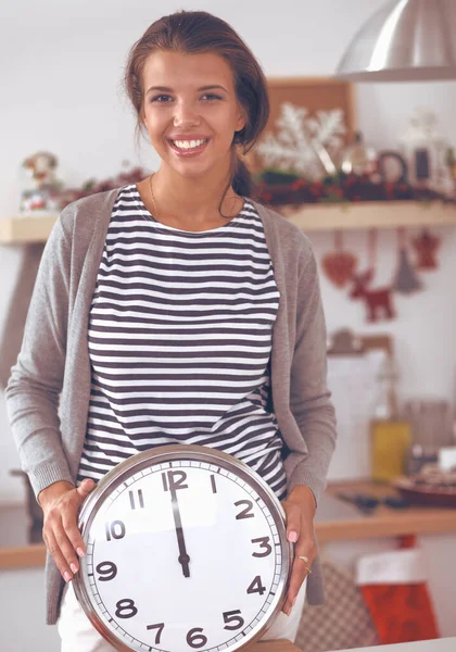 Gelukkig jong vrouw tonen klok in kerst versierd keuken — Stockfoto