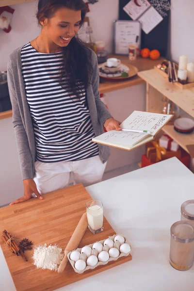 Glimlachende jonge vrouw in de keuken, geïsoleerd op kerst achtergrond — Stockfoto