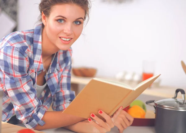 Jovem mulher lendo livro de receitas na cozinha, à procura de receita — Fotografia de Stock