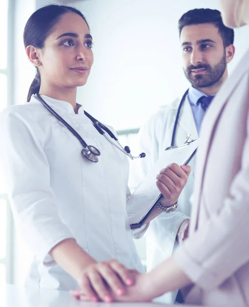 Handsome doctor is talking with young female patient and making notes while sitting in his office — Stock Photo, Image