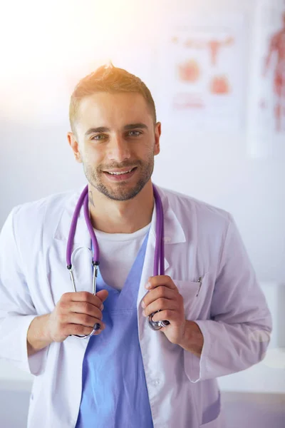 Retrato médico masculino joven y confiado de pie en el consultorio médico. — Foto de Stock