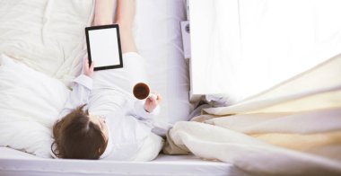 Sabahları yatakta otururken tablet kullanan ve kahve içen kadın portresi