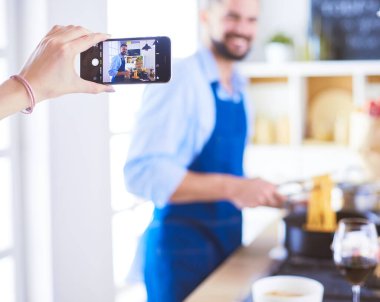 Adam ev mutfağında lezzetli ve sağlıklı yemekler hazırlıyor. Blogu için video çekiyor..
