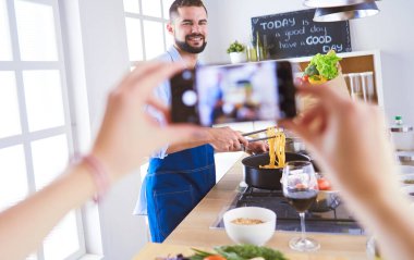 Adam ev mutfağında lezzetli ve sağlıklı yemekler hazırlıyor. Blogu için video çekiyor..