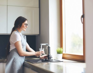 Bir bardak suyu paslanmaz çelikten, krom musluktan ya da musluktan dolduran kadın.