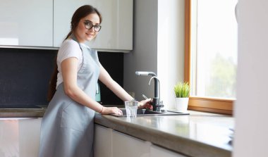 Bir bardak suyu paslanmaz çelikten, krom musluktan ya da musluktan dolduran kadın.