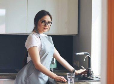 Bir bardak suyu paslanmaz çelikten, krom musluktan ya da musluktan dolduran kadın.
