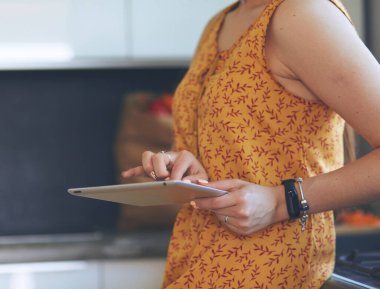 Mutfaktaki genç, beyaz tenli esmer ev kadınının portresi. Sabah bir fincan kahve ve tabletle