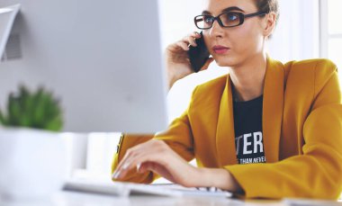 İş kadını ofiste bilgisayar ve cep telefonu kullanarak işine konsantre oluyor.