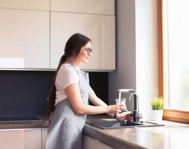 Bir bardak suyu paslanmaz çelikten, krom musluktan ya da musluktan dolduran kadın.