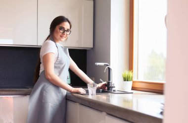 Bir bardak suyu paslanmaz çelikten, krom musluktan ya da musluktan dolduran kadın.