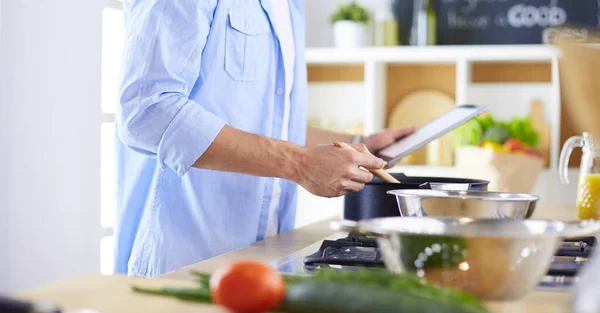 Man following recipe on digital tablet and cooking tasty and healthy food in kitchen at home