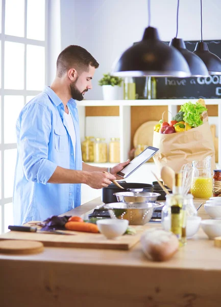 Man following recipe on digital tablet and cooking tasty and healthy food in kitchen at home — Stock Photo, Image