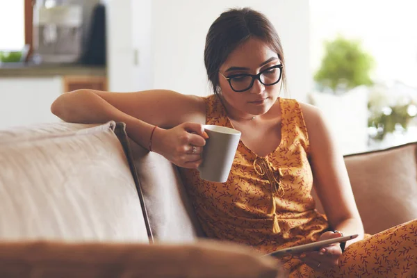 Молодая женщина использует планшет во время отдыха дома с кофе на диване — стоковое фото