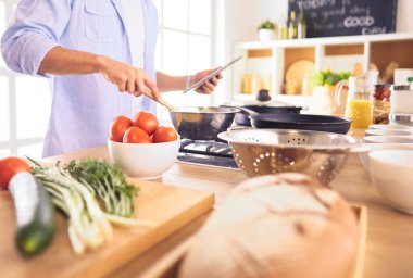 Dijital tablet ve yemek pişirme tarifine uyan bir adam evdeki mutfakta lezzetli ve sağlıklı yemekler pişiriyor.