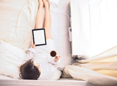 Sabahları yatakta otururken tablet kullanan ve kahve içen kadın portresi
