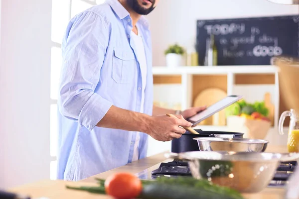 Manusia mengikuti resep pada tablet digital dan memasak makanan lezat dan sehat di dapur di rumah — Stok Foto
