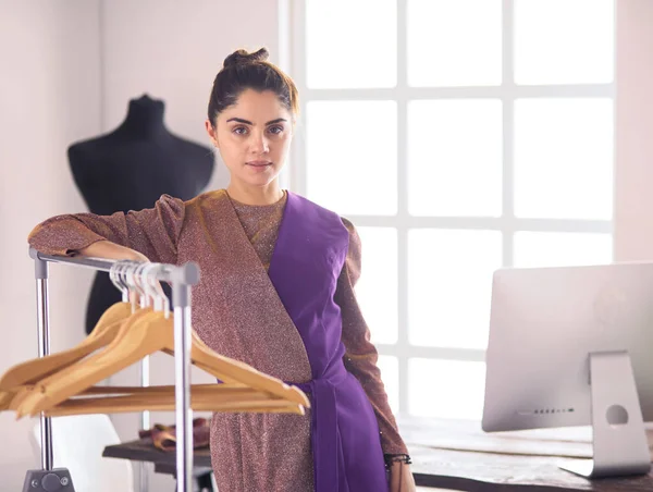 Beautiful young stylist near rack with hangers