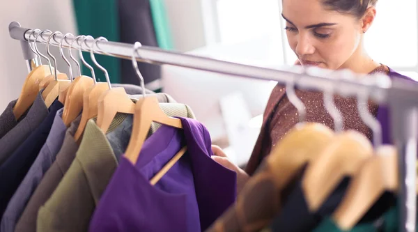 Beautiful young stylist near rack with hangers — Stock Photo, Image