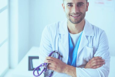 Genç ve kendinden emin erkek doktor portresi tıp ofisinde duruyor..