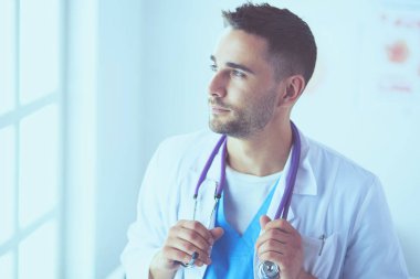 Genç ve kendinden emin erkek doktor portresi tıp ofisinde duruyor..