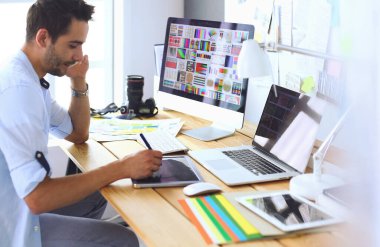 İnternette çalışırken bilgisayarın ve dizüstü bilgisayarın önünde grafik stüdyosunda oturan genç tasarımcının portresi.