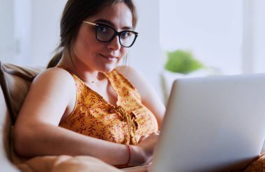 Evde dizüstü bilgisayar üzerinde çalışan kanepede oturan genç kadın