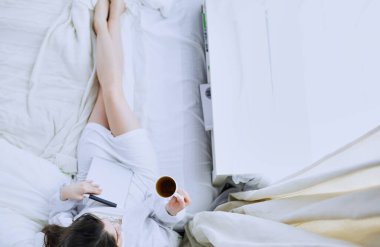 Sabahları yatakta otururken tablet kullanan ve kahve içen kadın portresi