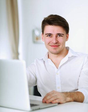 Yakışıklı genç adam dizüstü bilgisayarda oturuyor ve çalışıyor.