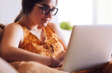 Evde dizüstü bilgisayar üzerinde çalışan kanepede oturan genç kadın