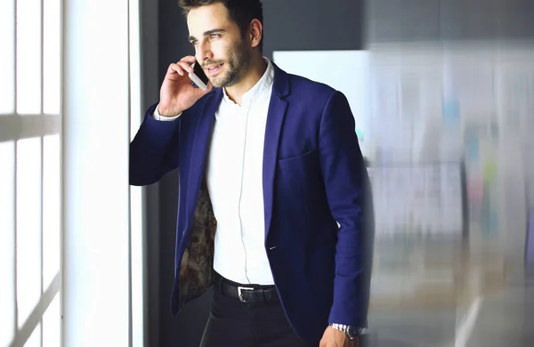 Homem de negócios de terno falando ao telefone e olhando para longe perto da janela . — Fotografia de Stock