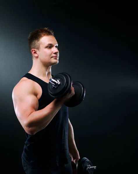 Primer plano de un joven musculoso levantando pesas sobre fondo oscuro — Foto de Stock