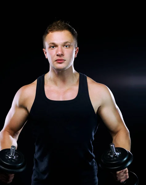 Närbild av en muskulös ung man lyfta vikter på mörk bakgrund — Stockfoto