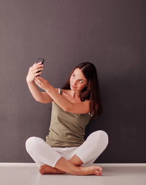 Sorridente donna bruna seduta sul pavimento e fare selfie su smartphone — Foto Stock