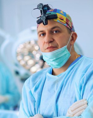 Ameliyat odasında arka planda erkek cerrah var.